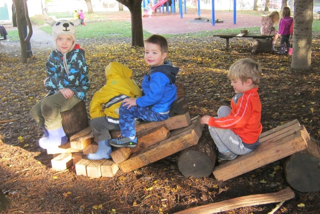 Young children play on wooden logs and stumps on the playground