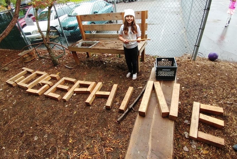 A child stands behind her name spelled out in wooden letters on the playground