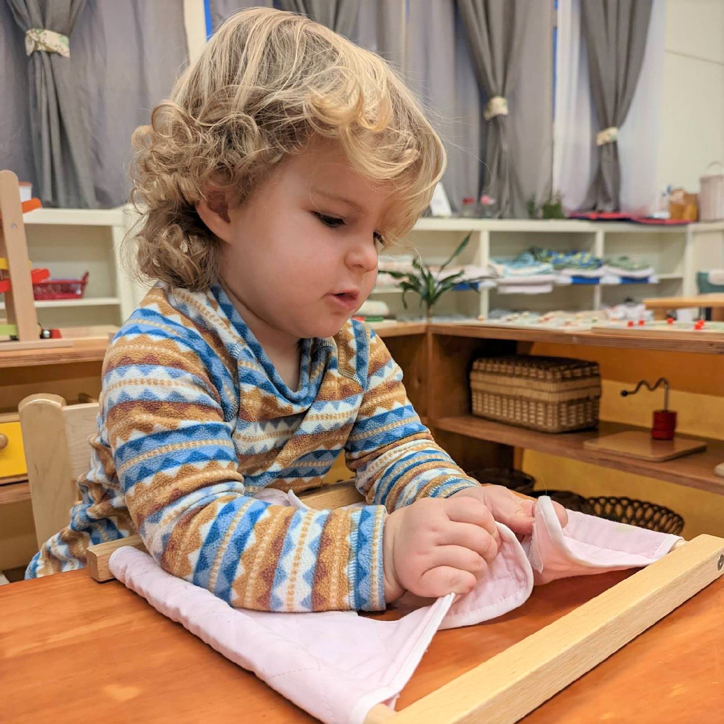 A young child smooths a folded cloth on a tray