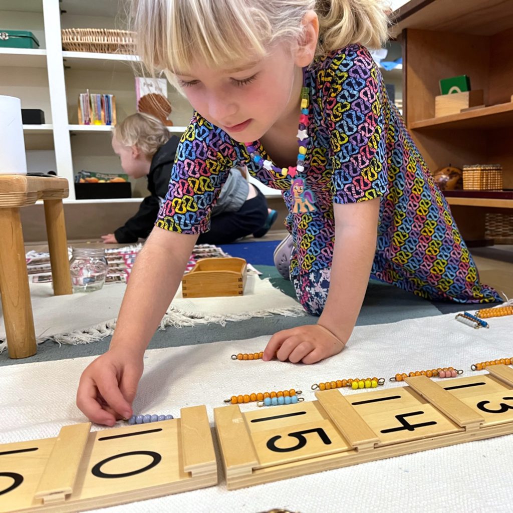 A student works with beautiful wooden Montessori math materials to learn the concept of teen numerals