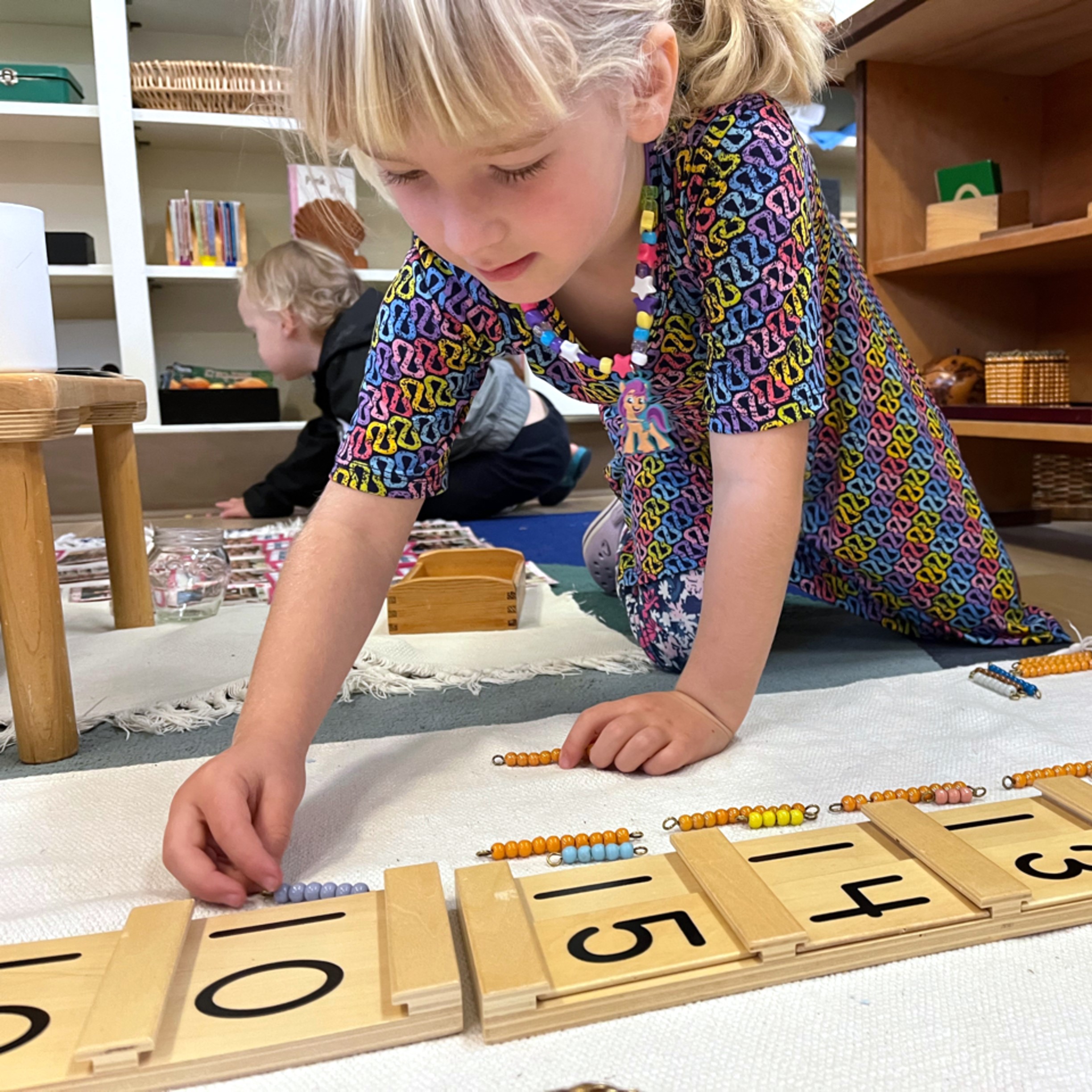 A student works with beautiful wooden Montessori math materials to learn the concept of teen numerals