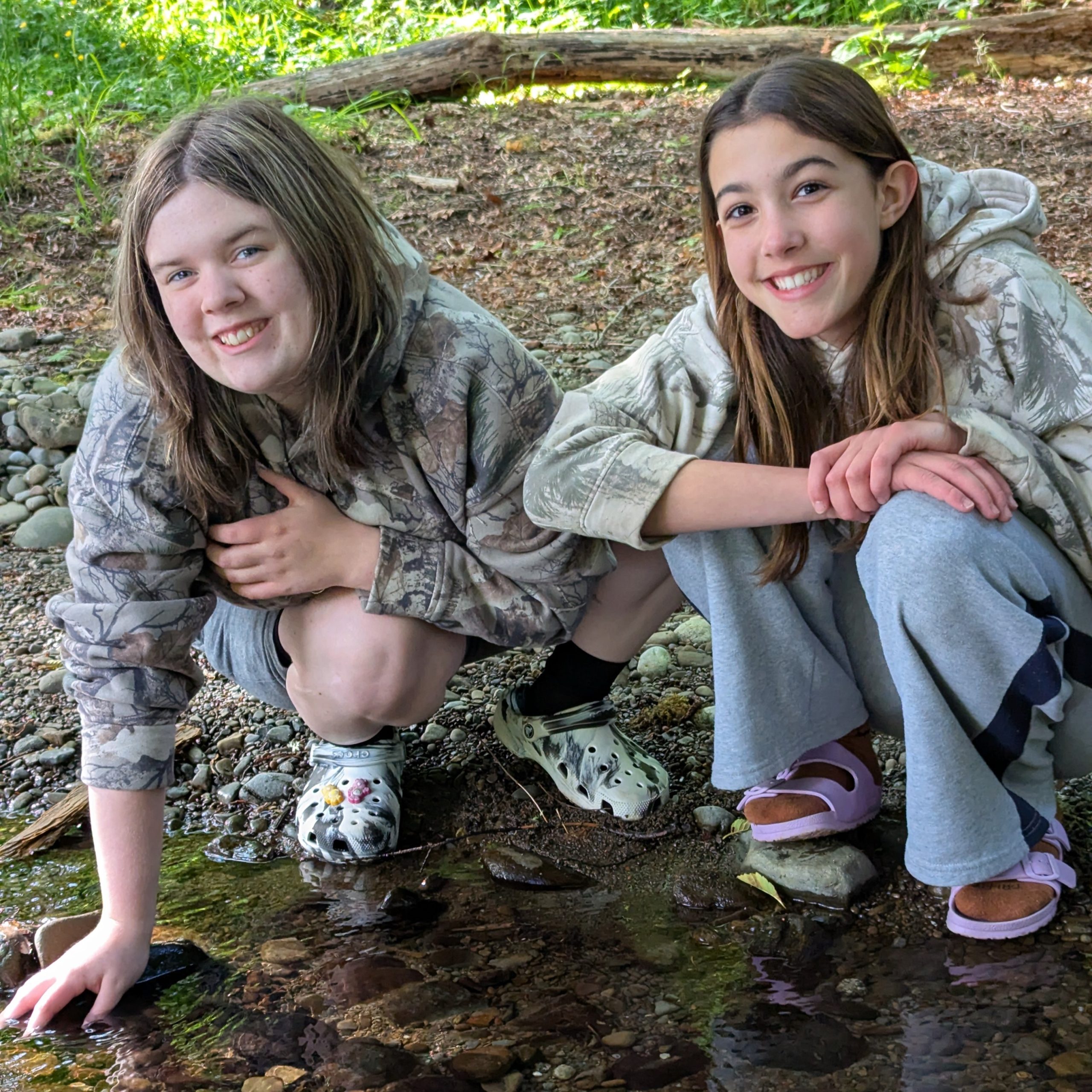 Two middle school students crouch by a stream and smile