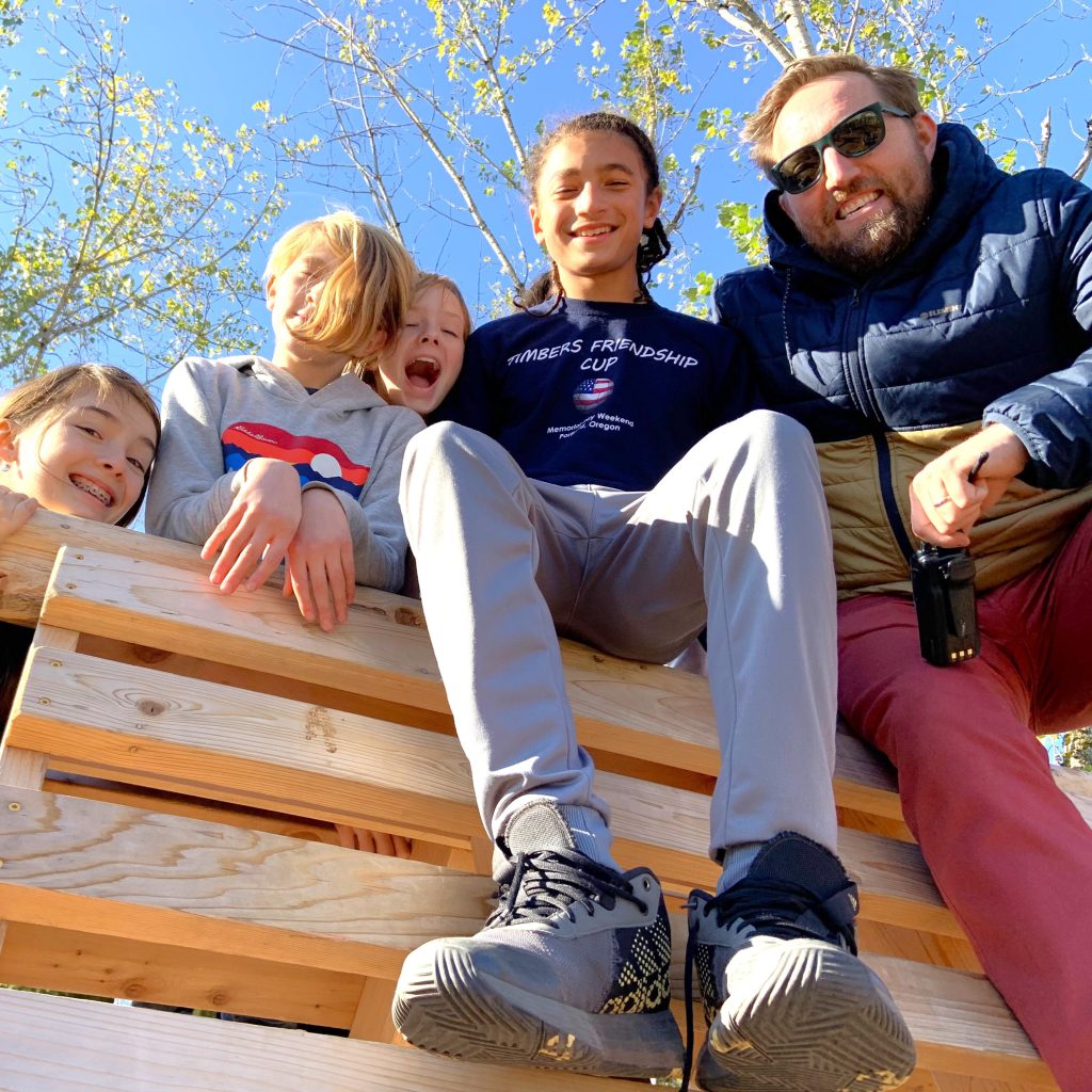 Students and a teacher sit together on wooden pallets outdoors