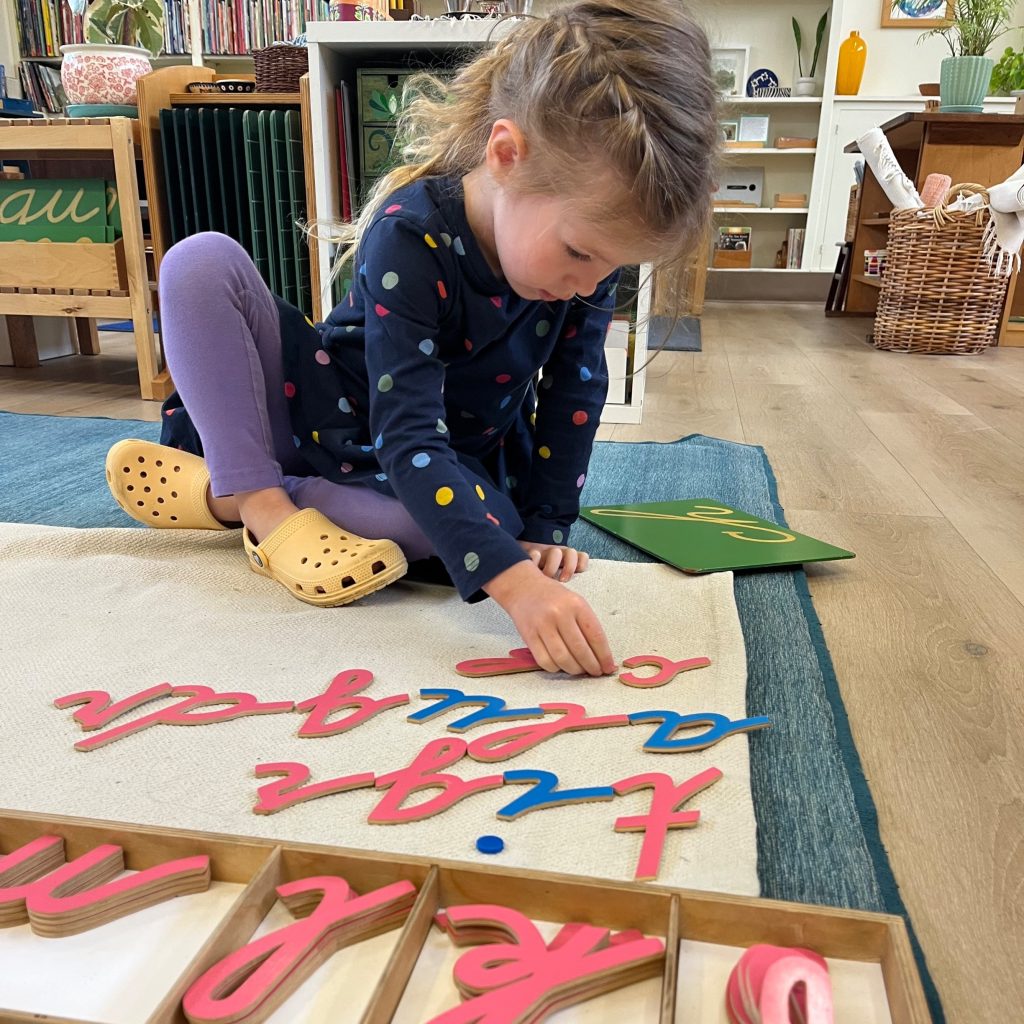 a students sits on a rug an builds words with the Montessori moveable alphabet material
