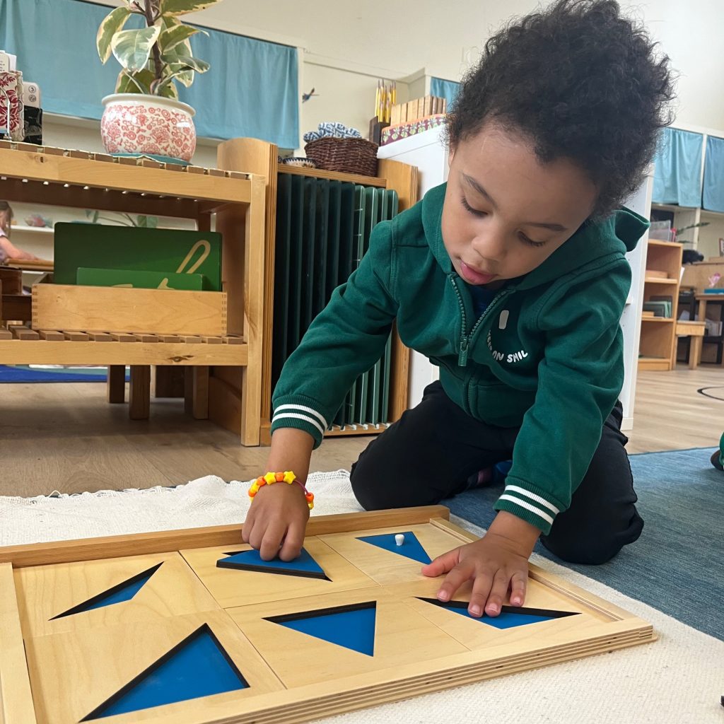 A student kneels in front of a rug with a wooden geometry puzzle of the six types of triangles