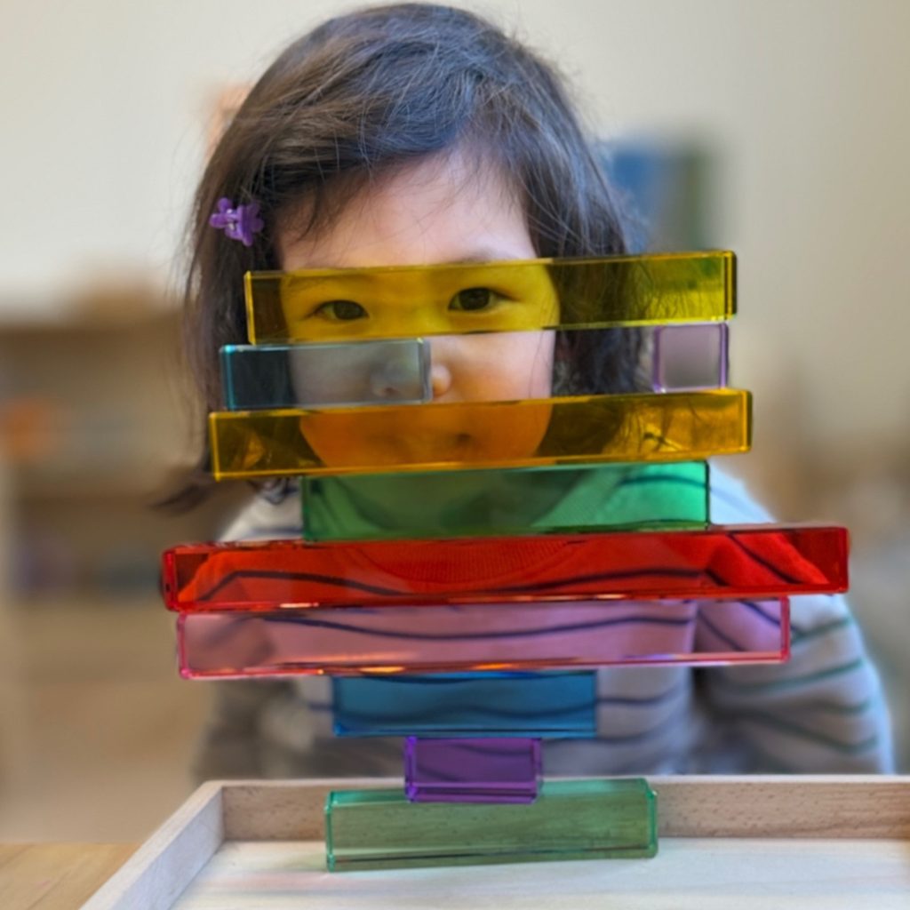 A young child peers over a stack of colorful translucent blocks