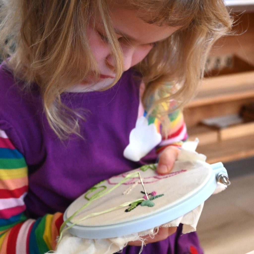 A student carefully embroiders a flower with deep concentration, focus, and creative expression while mastering fine motor control.