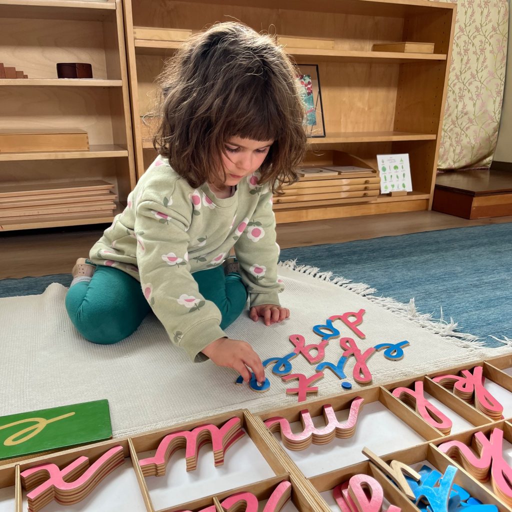 a 4 year old sits on the rug and spells out words with a wooden alphabet